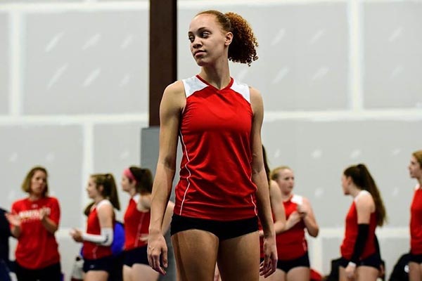 A girl in a red volleyball jersey smiles while looking off to the side during volleyball training